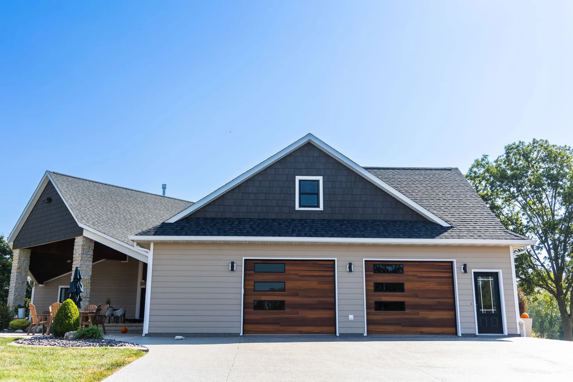 Tan house with two cedar-tone plank garage doors and a dark shingled gable