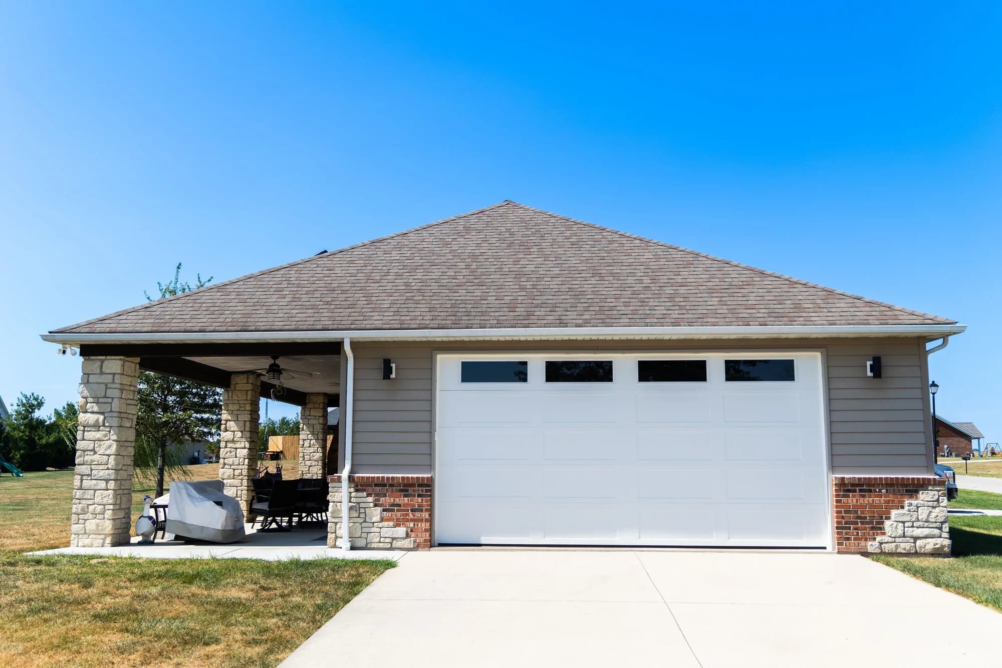 White garage door with top windows on a tan house with a covered stone patio