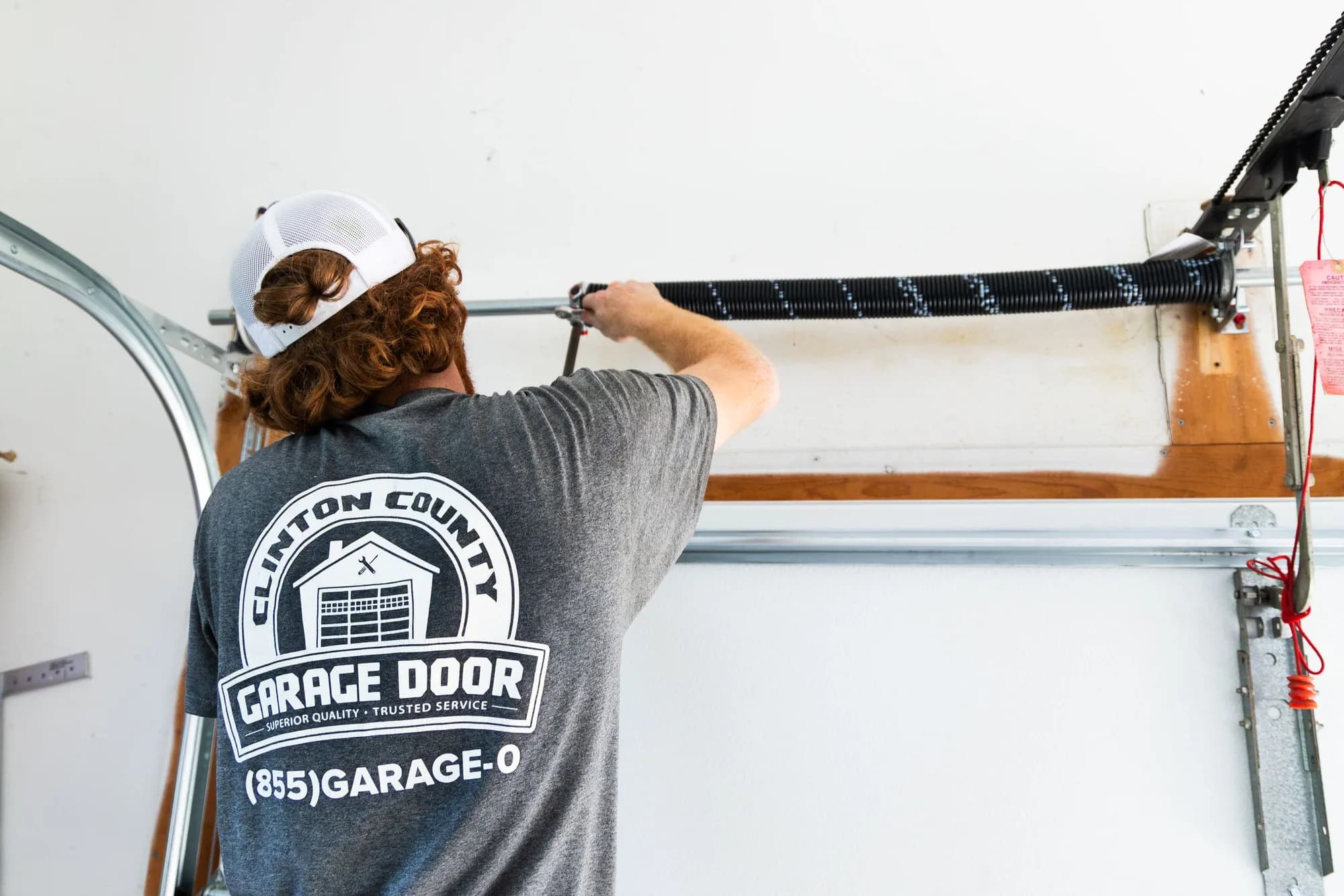 Technician in a CC Garage Door shirt checking a torsion spring above a garage door