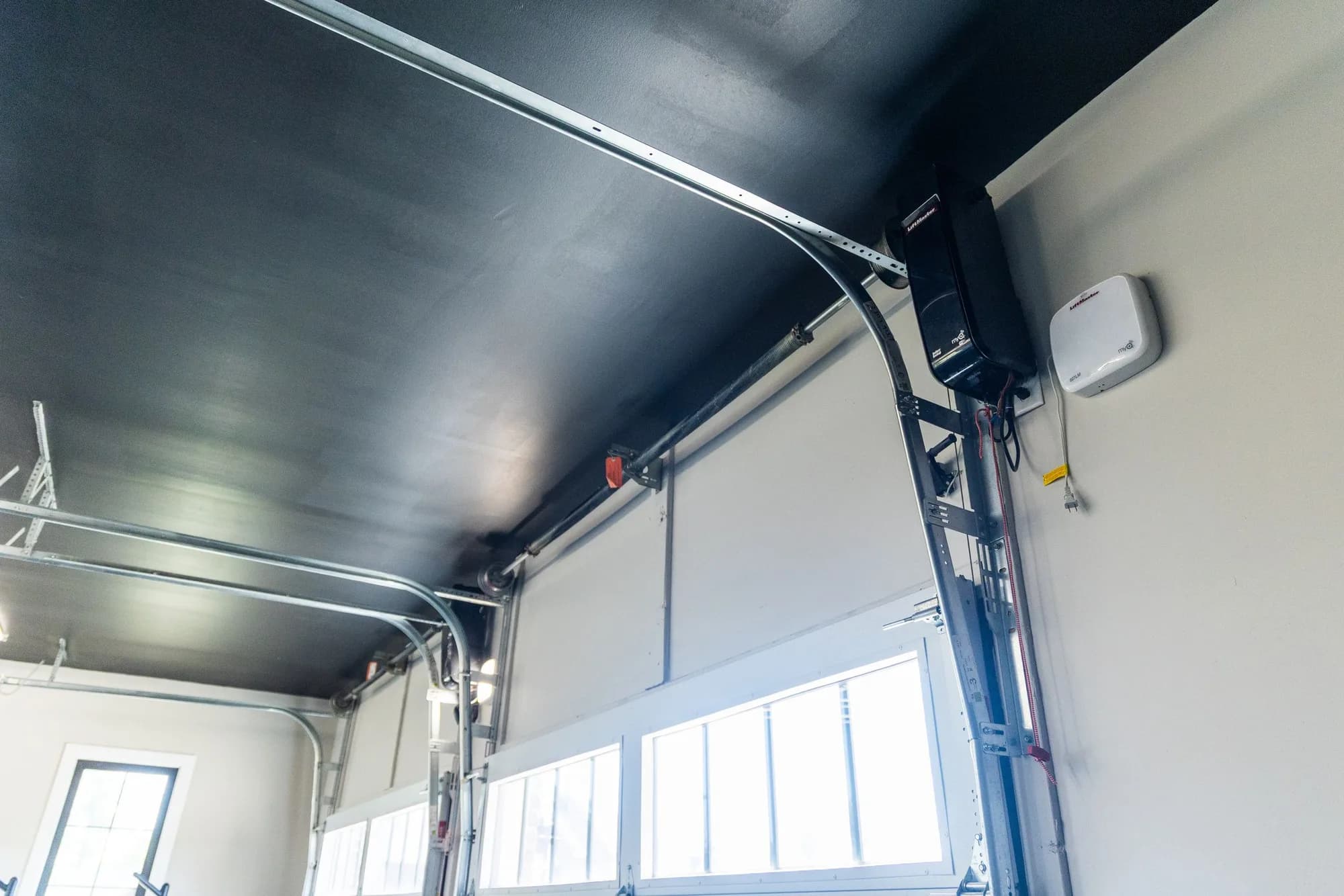 Inside a garage looking at two white sectional doors with wall-mounted openers and the torsion shaft above