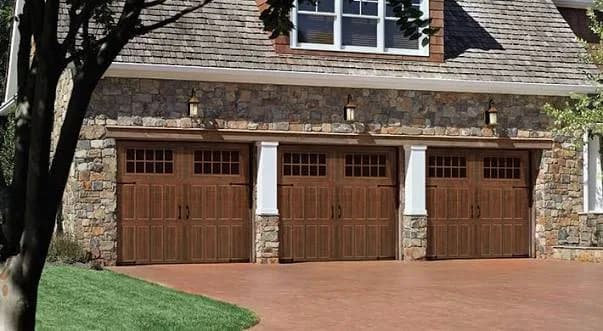 Amarr Hillcrest carriage-house garage doors in a stained wood finish with glazed top windows on a stone-faced home