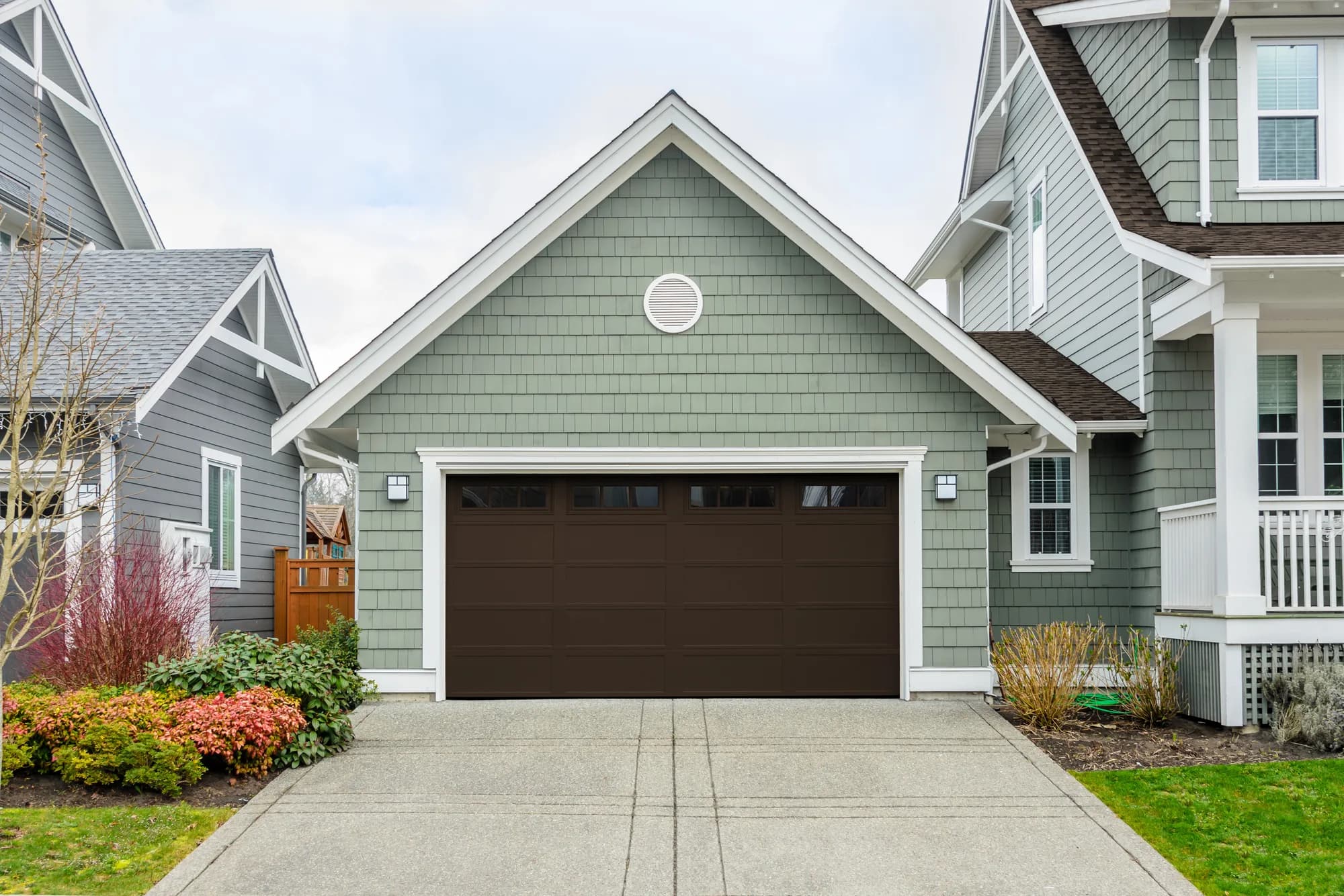 Dark brown recessed long-panel Haas garage door with top windows on a green shake-sided garage