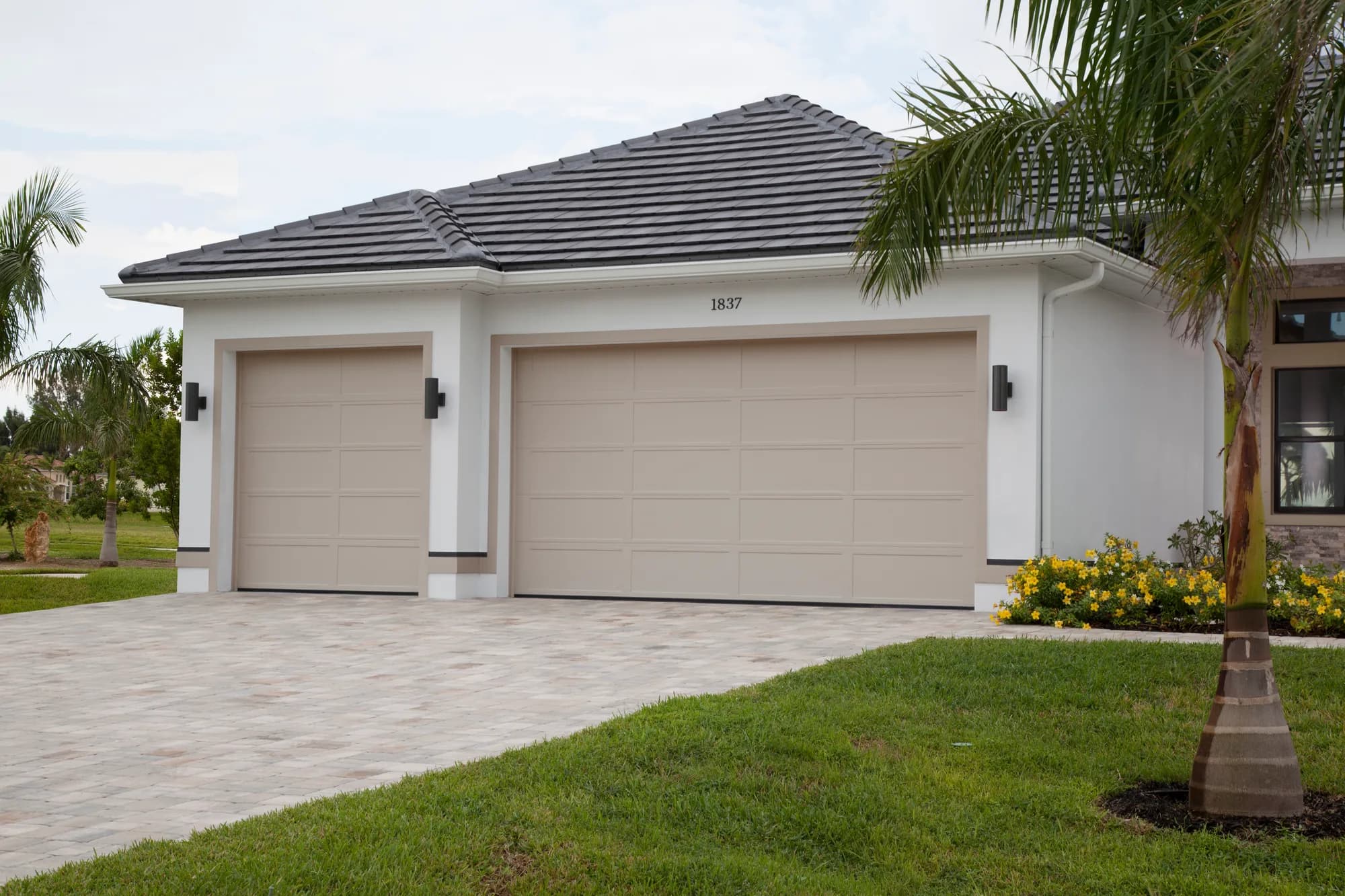 Tan recessed long-panel Haas garage doors, a single and a double, on a white stucco home