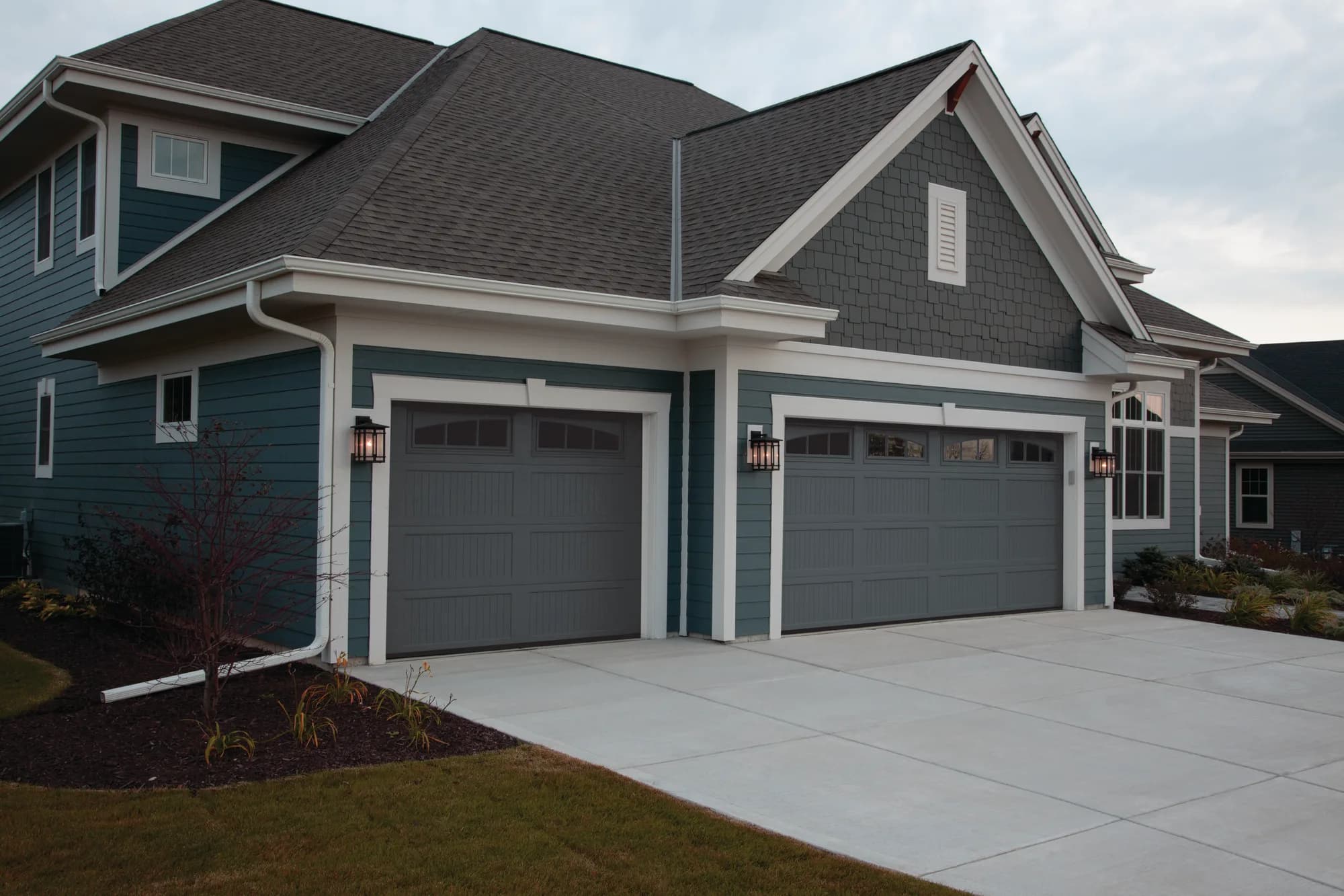 Two black carriage-style Haas garage doors with arched top windows on a blue-grey craftsman home at dusk