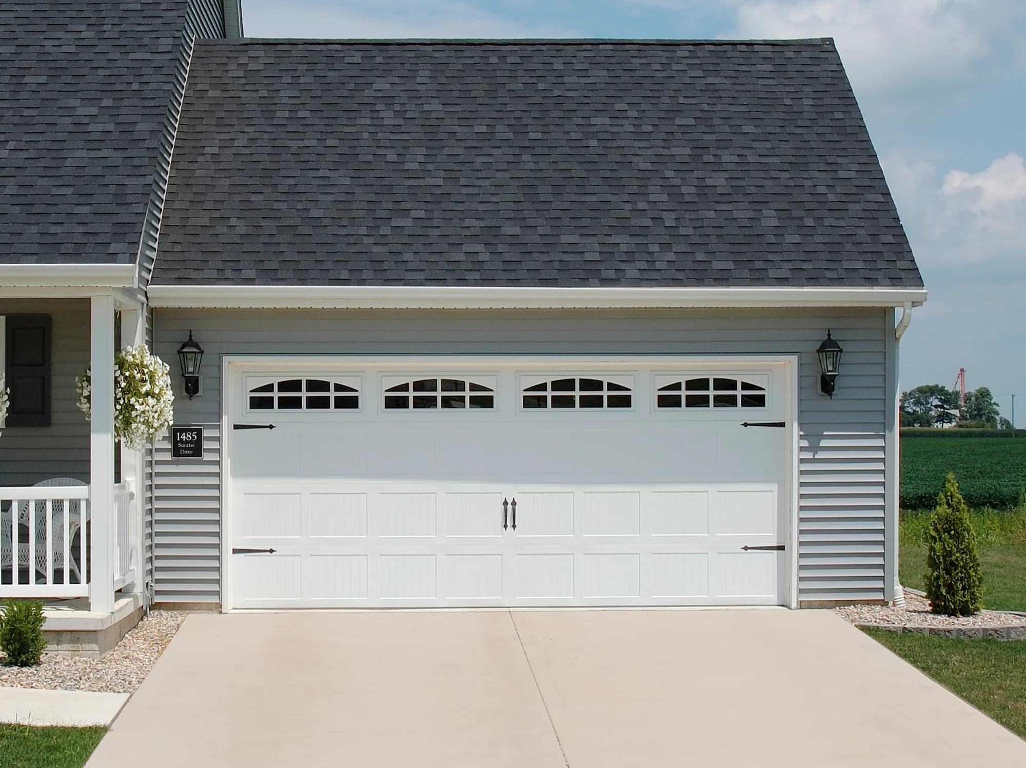 White stamped carriage-house garage door with arched top windows and black hinge hardware on a grey vinyl-sided house
