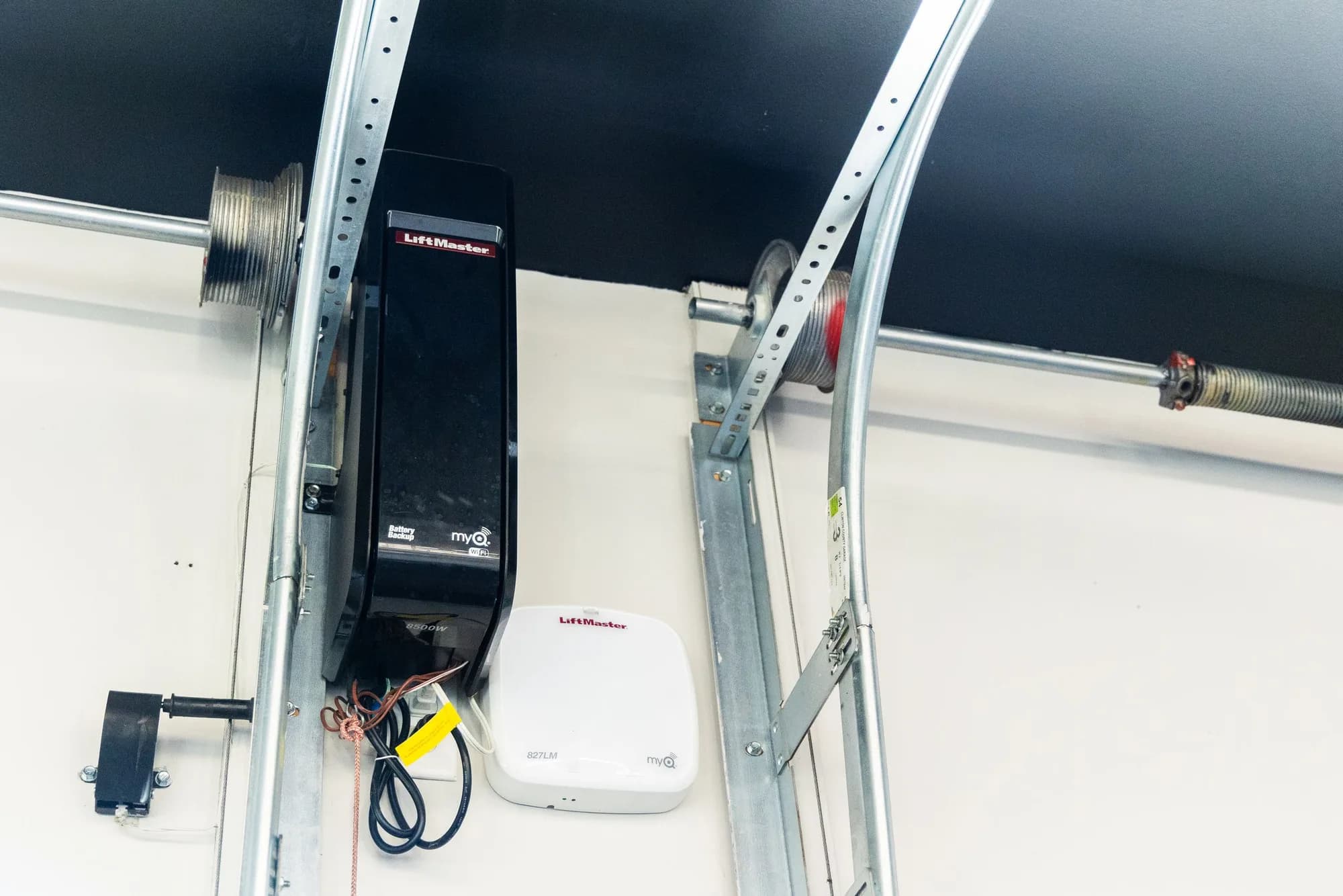 LiftMaster wall-mount jackshaft opener beside the vertical door track, with a myQ hub on the wall