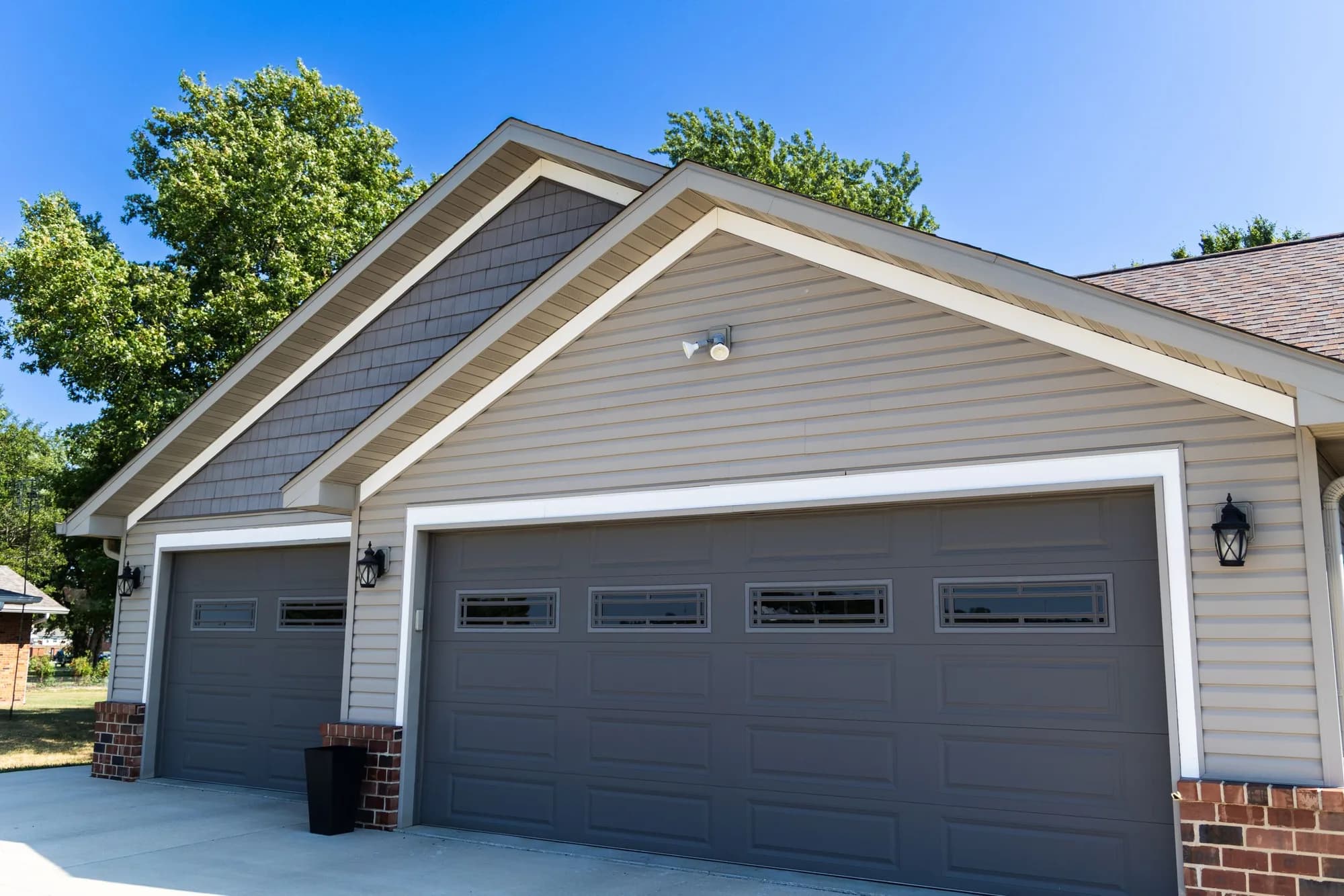 Tan two-story home with a taupe long-panel garage door and a row of top windows, seen from the driveway