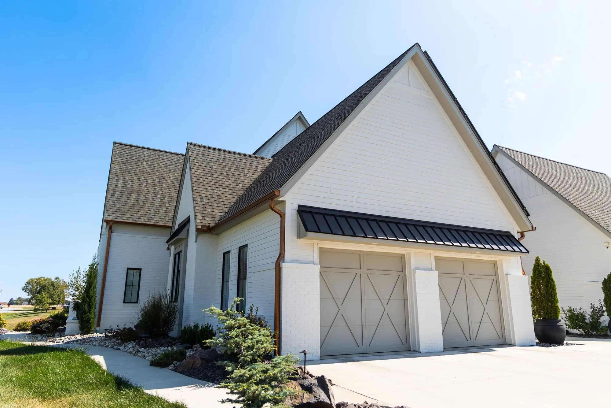 White painted brick home with two carriage overlay garage doors under a black metal awning