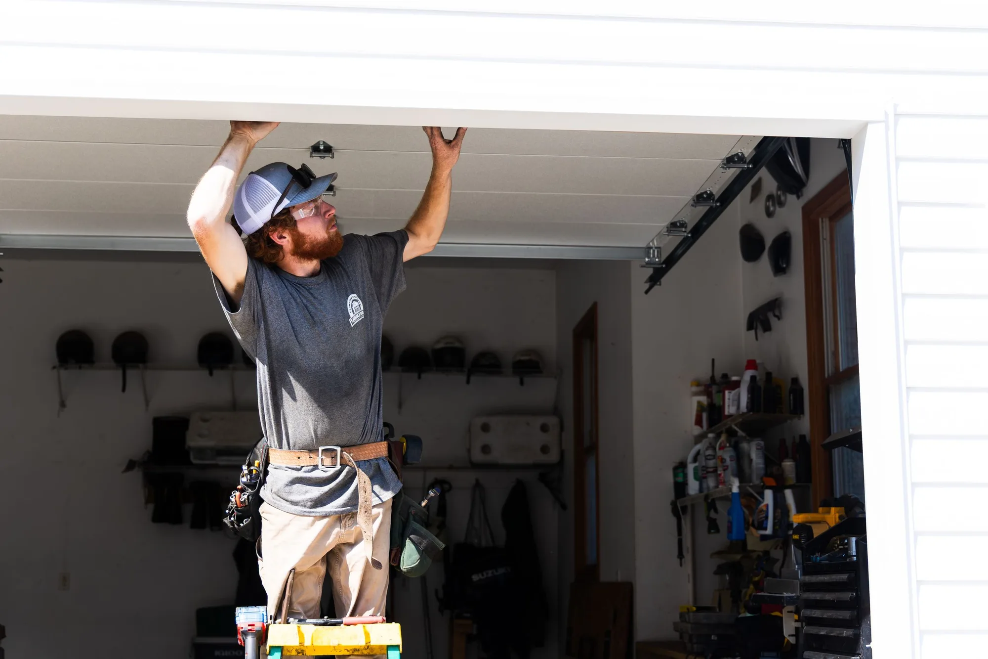 Technician on a ladder working on the garage door opener from inside the garage