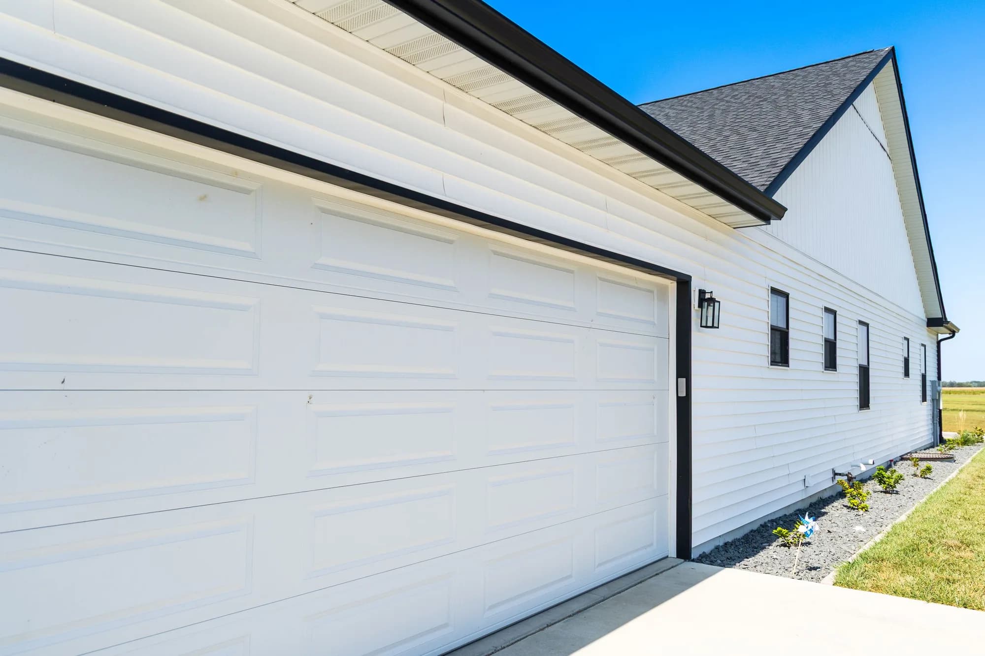 White long-panel garage door seen from the side on a white-sided house, with its sections and bottom seal in view