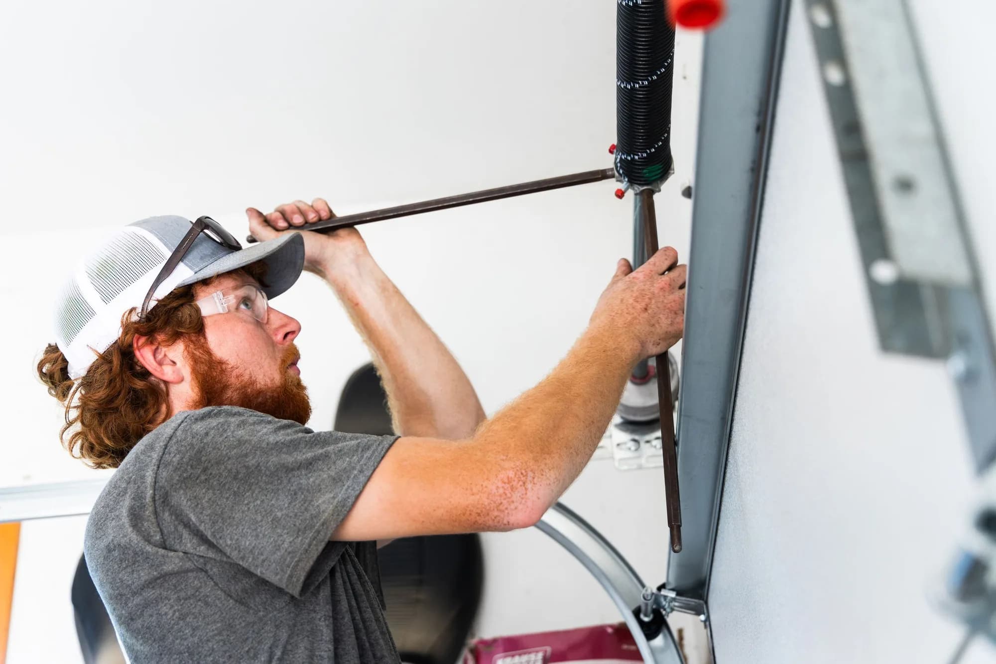 Technician winding a torsion spring with winding bars above a garage door