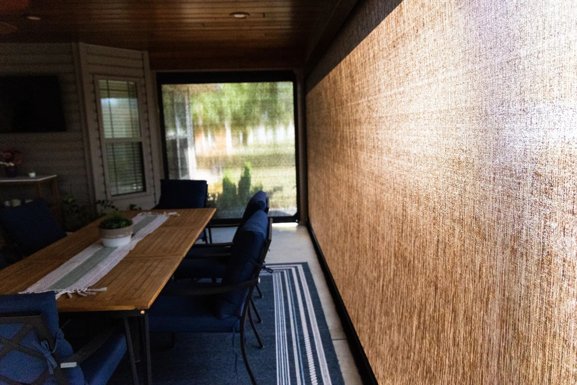 Close view of a lowered mesh screen seated in its side track, with a patio dining table behind it